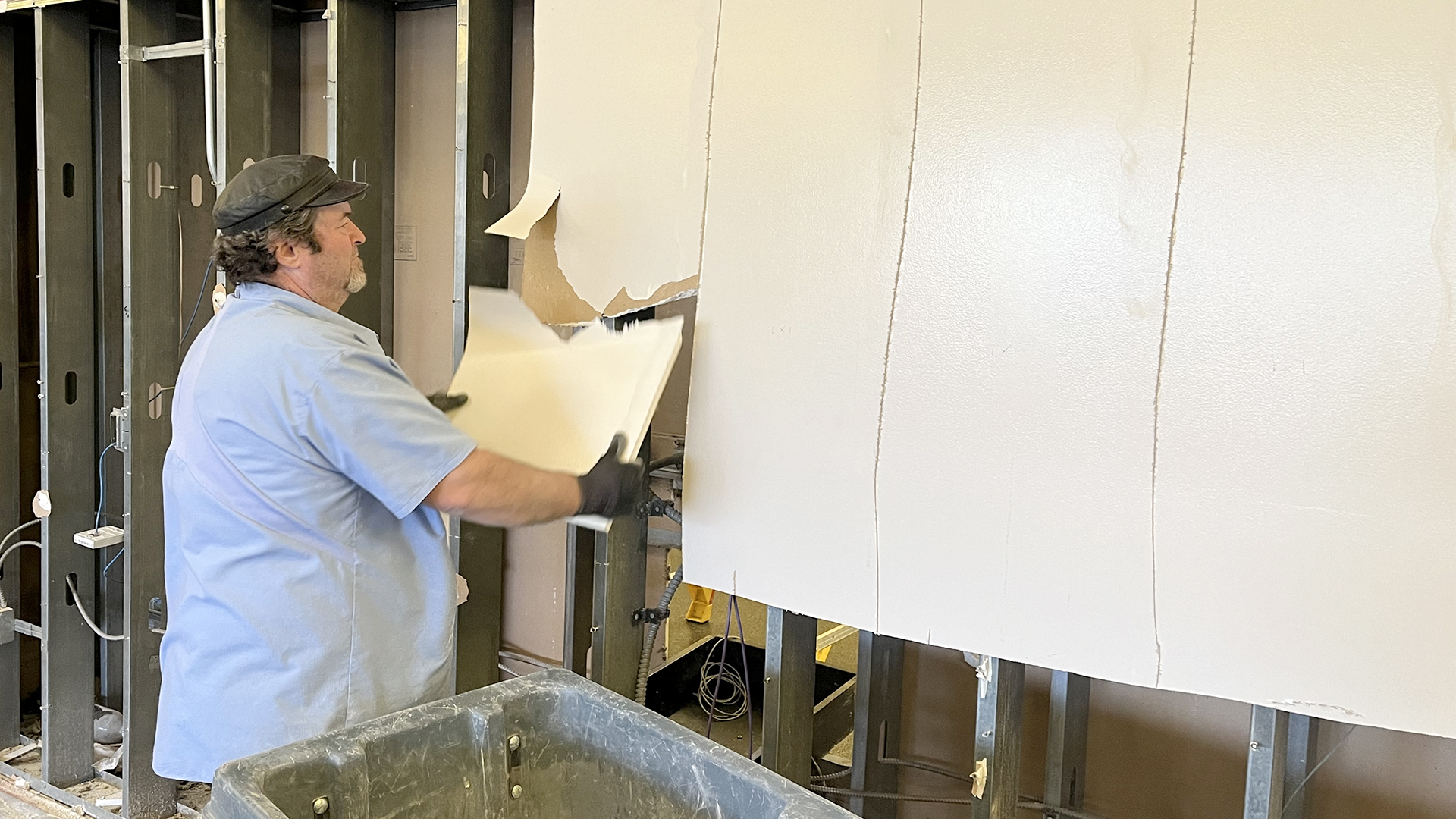 A worker takes off sheetrock from the wall separating the cardio and weight rooms.