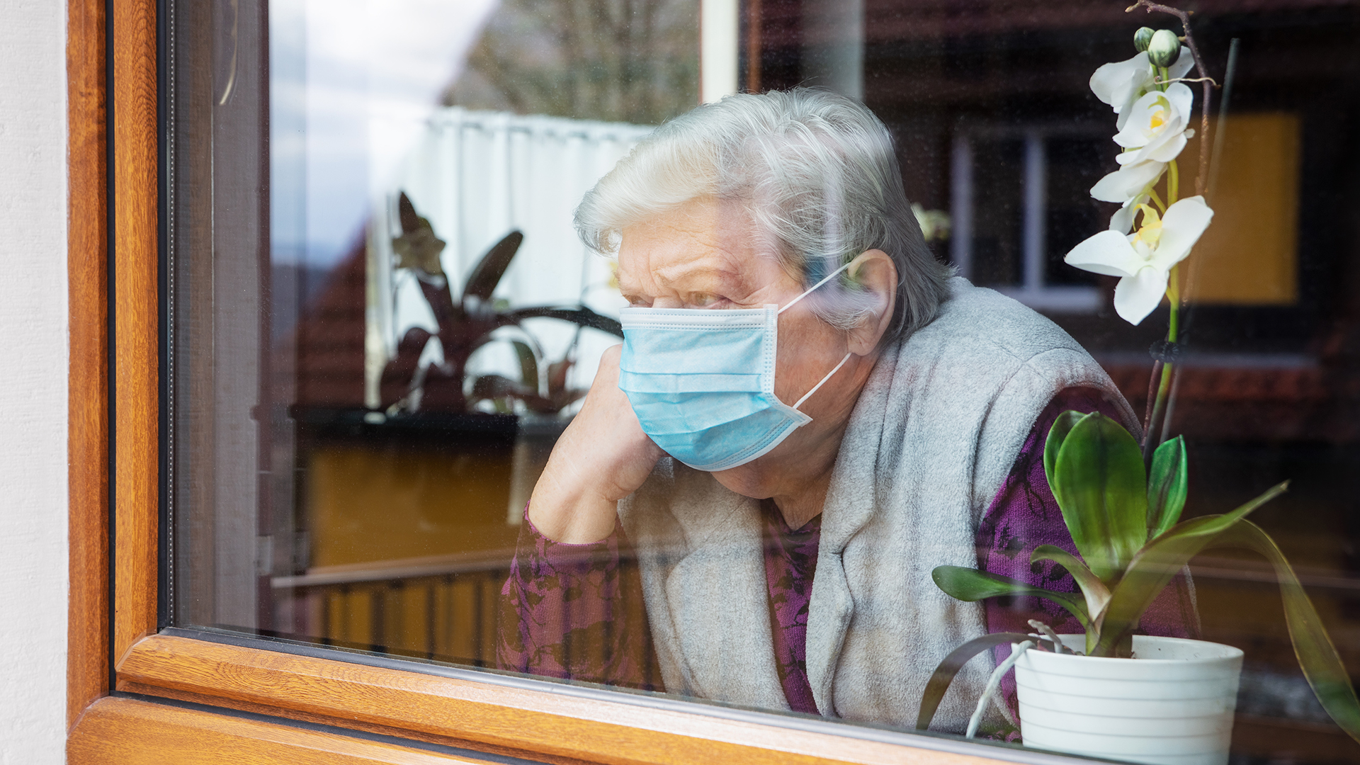 A senior in a mask stares out her window