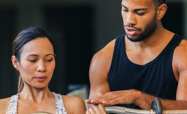 male training coach assisting female weight lifter