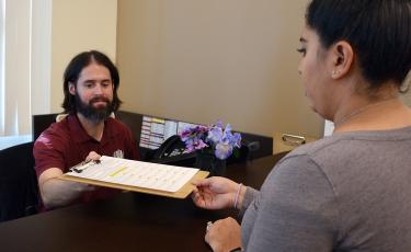 man at counter handing out sign-up sheet to woman