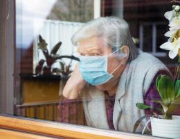 A senior in a mask stares out her window